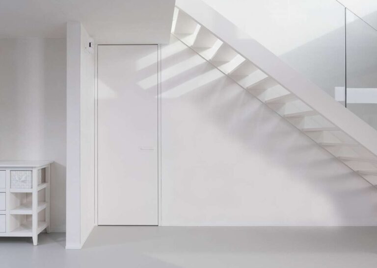 supermooie witte blokdeur in een wit interieur onder een trap