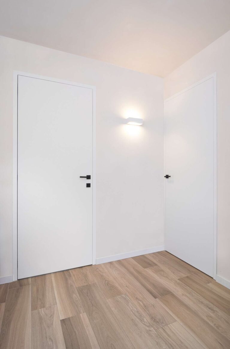 Twee prachtige moderne witte binnendeuren met een zwarte deurklink met laminaat als vloer
